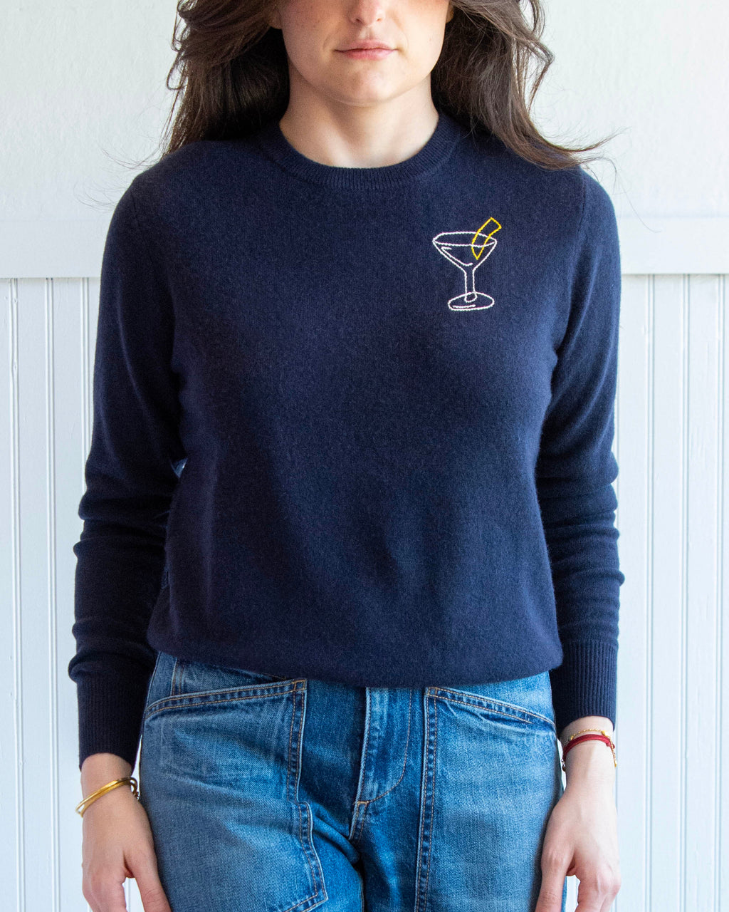 Person wearing a navy blue sweater with a martini glass design and blue jeans against a white background